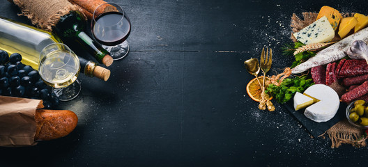 A bottle of wine, cheeses and traditional sausages on a wooden background. Brie cheese, blue cheese, gorgonzola, fuete, salami. Free space for text. Top view.