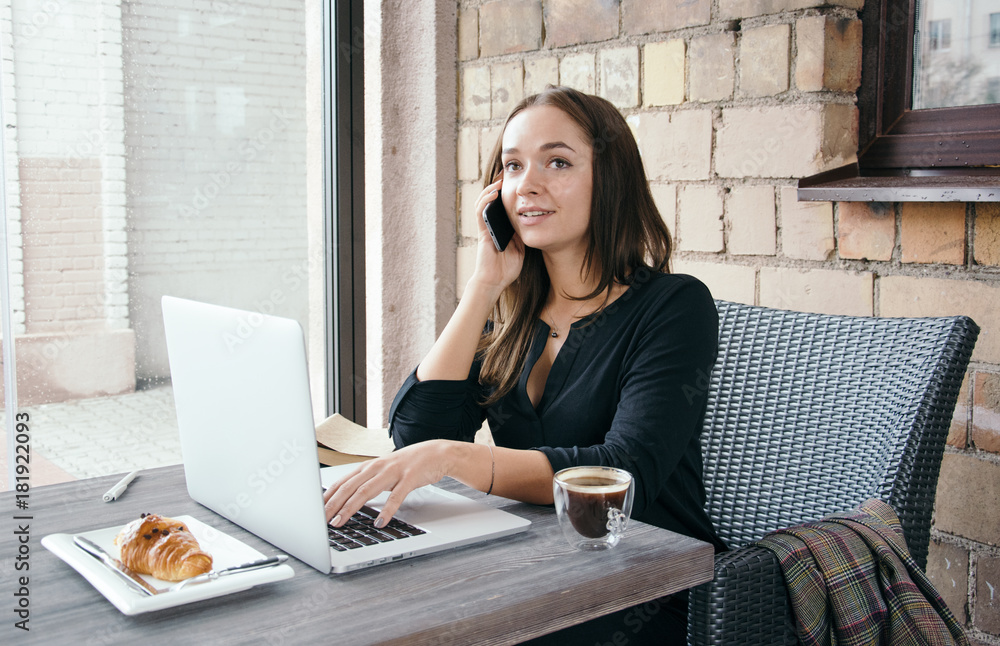 Young attractive woman sitting in a cafe in the morning before her work and planning tasks for the whole day. Beautiful lady talking on the phone and discussing business strategies with her colleague. Young attractive woman sitting in a cafe in the morning before her work and planning tasks for the whole day. Beautiful lady talking on the phone and discussing business strategies with her colleague.