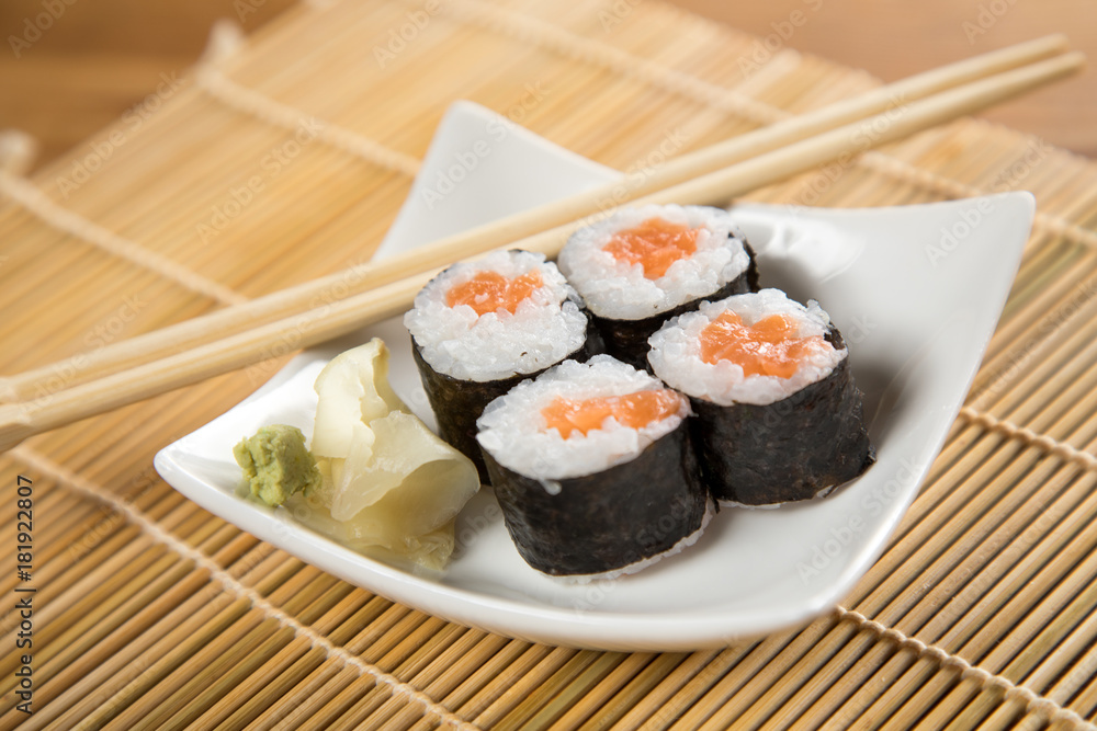 Vier Maki Sushi mit Lachs auf Teller an Holz Stäbchen Vier Maki Sushi mit Lachs auf Teller an Holz Stäbchen