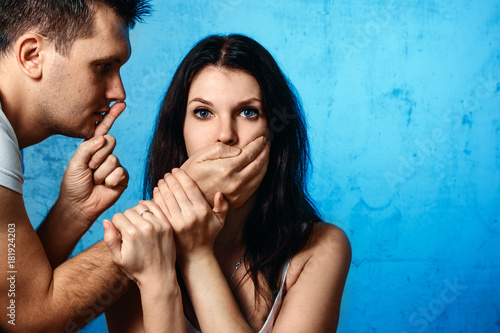 Fotografie A man closes his mouth against a woman against a blue wall