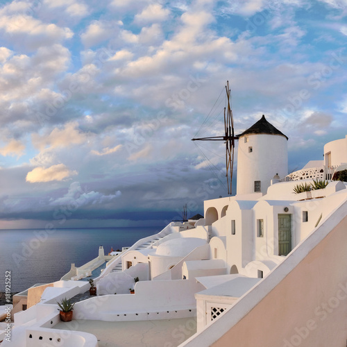 Traditional apartments and windmill in Oia village on a sunset, panoramic image