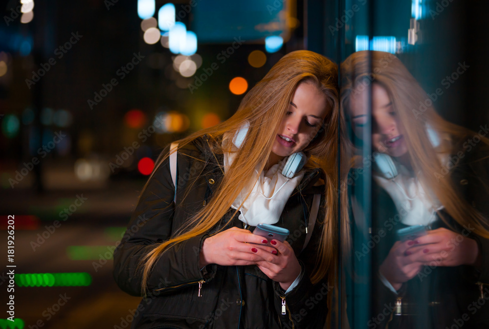 Woman with headphones using tablet waiting on bus stop at night in city