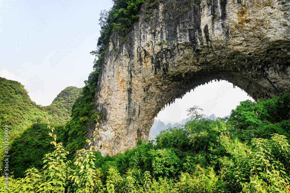 Natural arch in karst mountain among green woods. Moon Hill