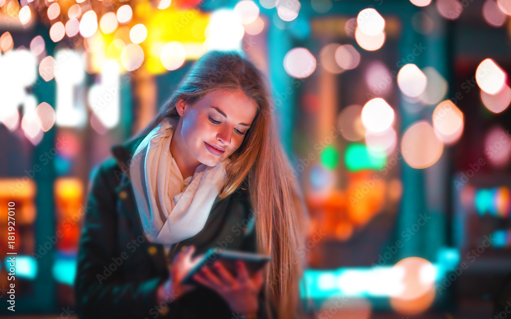 Girl in the city at night using tablet sitting on bench Girl in the city at night using tablet sitting on bench