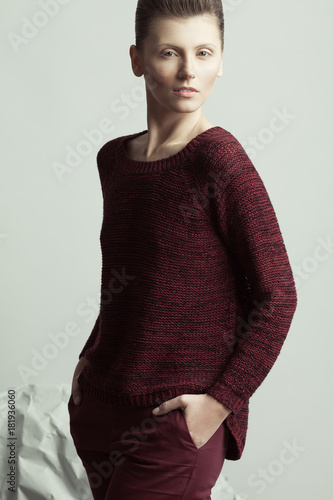 Art fashion, pret-a-porter concept. Portrait of androgynous model with short hair posing over gray background. Pale skin, natural make-up. Futurism style. Hands in pockets. Studio shot photo