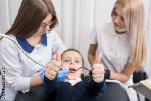Child showing thumbs up gestures of good class when female dentists examining and working on boy patient