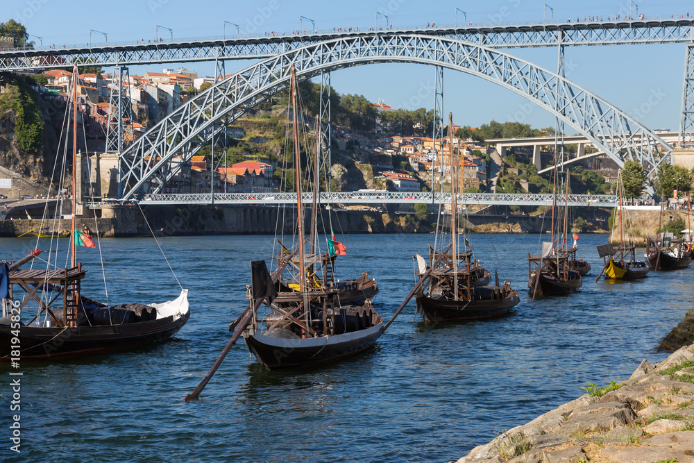 Traditional Rabelo Boats on the Bank of the River Douro and Dom Luis I Bridge in background - Porto, Portugal