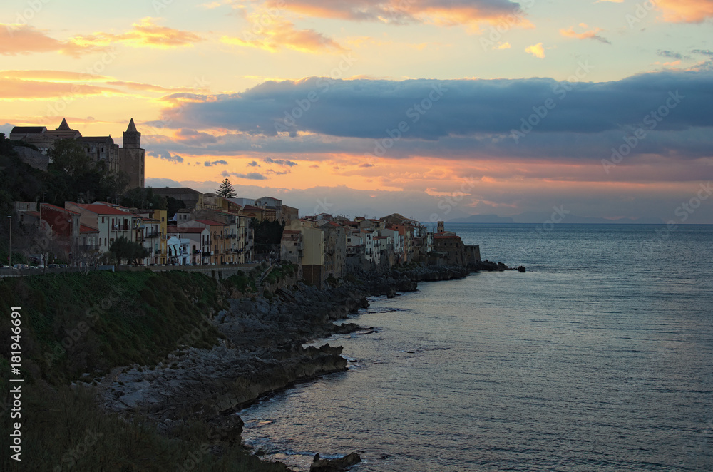 Village Cefalu houses on the cliffs and waves crashing rocks at sunset. Sicily, Italy