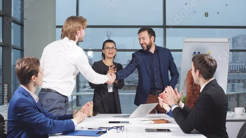 Business people shaking hands at interview while others clap at the office.