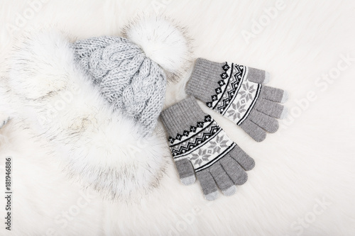 Winter knitted gloves and fur hat on white furry carpet.