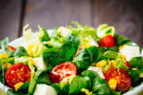 Dieting healthy salad  on rustic wooden table. Mixed greens, tomatos, diet cheese, olive oil and spices for healthy lifestyle concept.