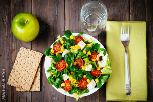 Dieting healthy salad and wholemeal bread toasts  on rustic wooden table. Mixed greens, tomatos, diet cheese, olive oil and spices for healthy lifestyle concept.