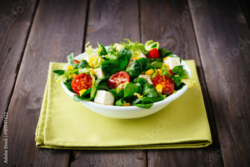 Dieting healthy salad  on rustic wooden table. Mixed greens, tomatos, diet cheese, olive oil and spices for healthy lifestyle concept.
