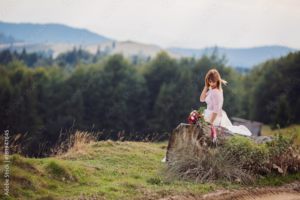 Lonely bride sits on the block on a mountain hill with her wedding bouquet