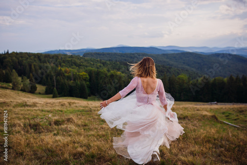 Gorgeous bride whirls on the hill before beautiful mountain landscape