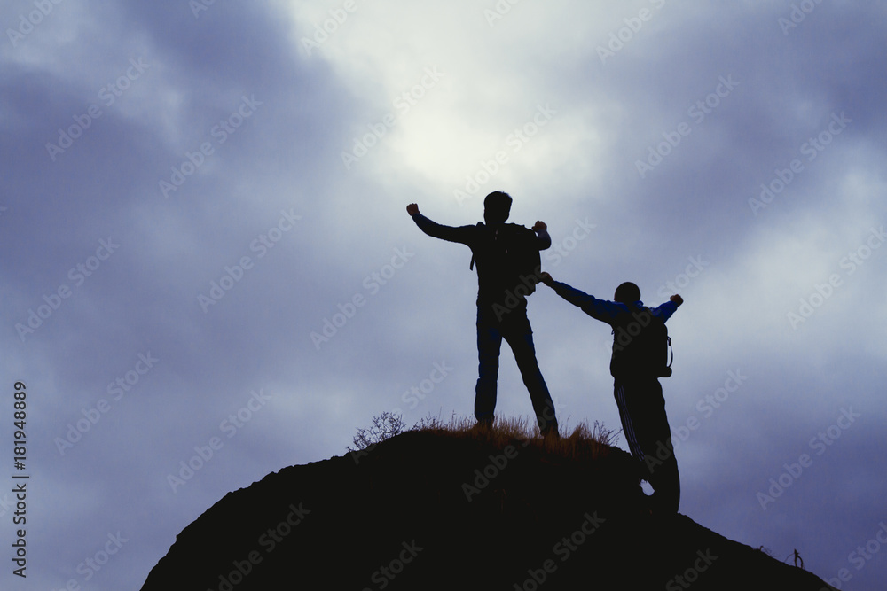 Silhouettes of two mountain climbers on the top of a mountain with victorious gesture.