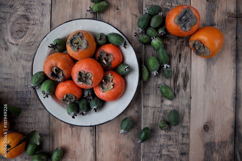 On the table in a plate or box a fresh persimmon, feijoa and citrus mandarins On the table in a plate or box a fresh persimmon, feijoa and citrus mandarins