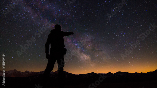 Person pointing at the milky way in a mountainous landscape.