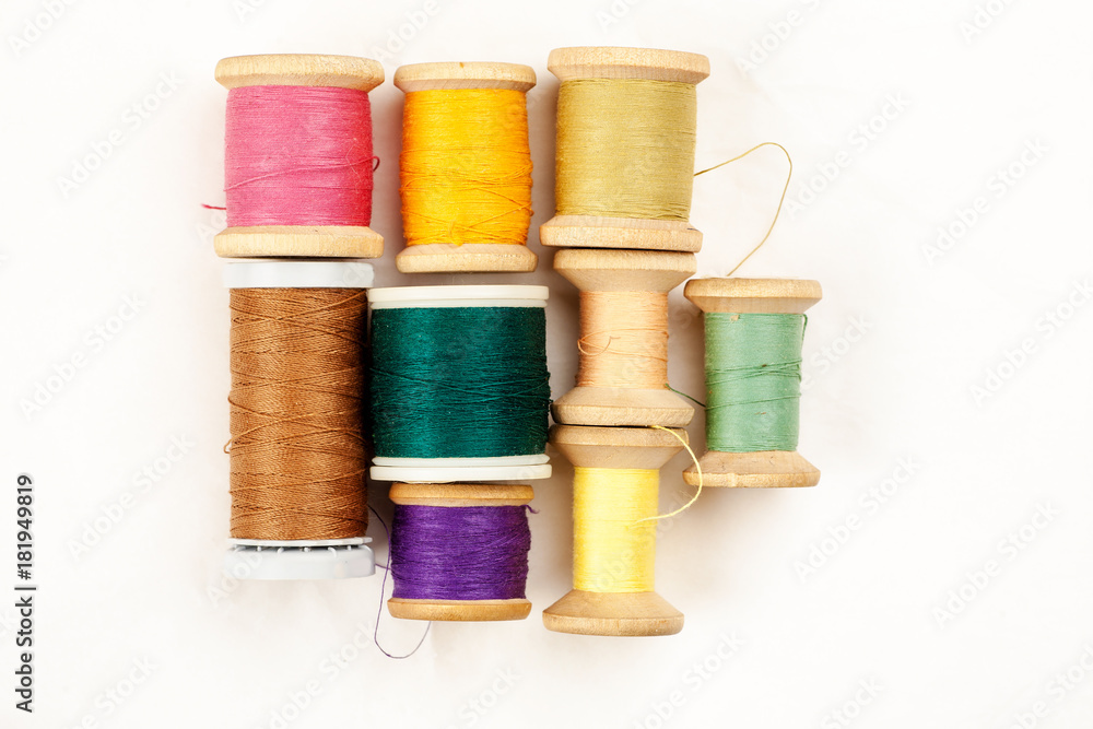 Different colour thread on wooden spools on a white background