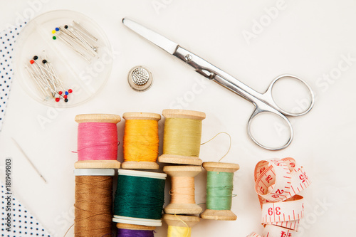 Set of tools and accessories for sewing and needlework with threads in spools, needles, measuring tape and other items on a white background