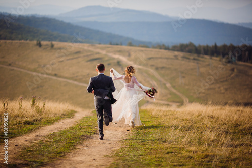 Bride and groom run on the hill before beautiful mountain landscape