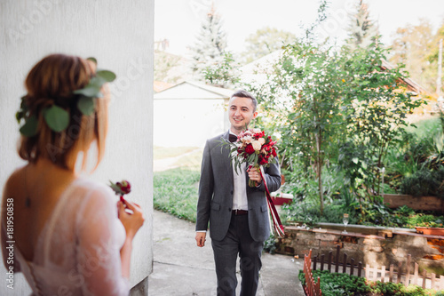 Look from behind bride's back at groom coming to her with wedding bouquet photo