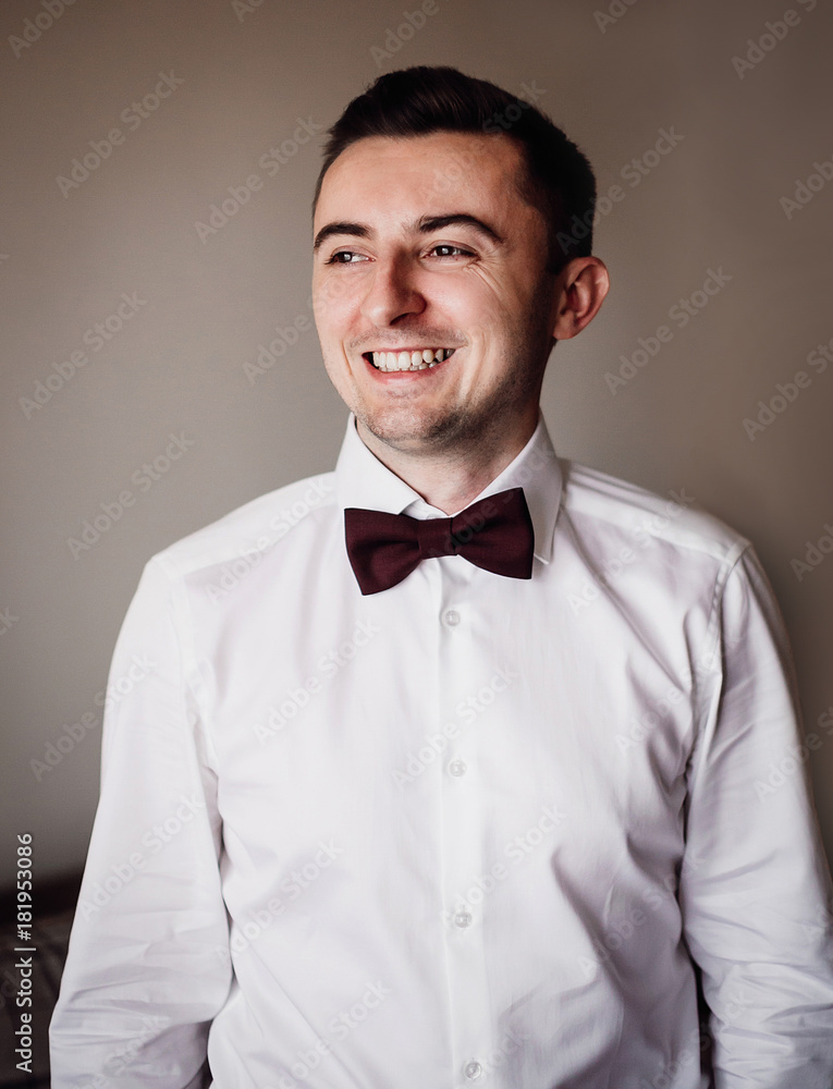 Groom puts on his shirt red bow tie standing in the room Groom puts on his shirt red bow tie standing in the room