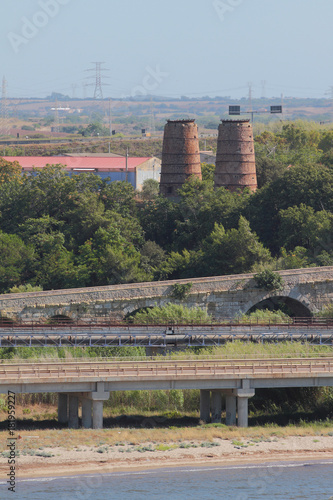 Automobile, railway and ancient Roman bridges on suburb of city. Porto-Torres, Italy