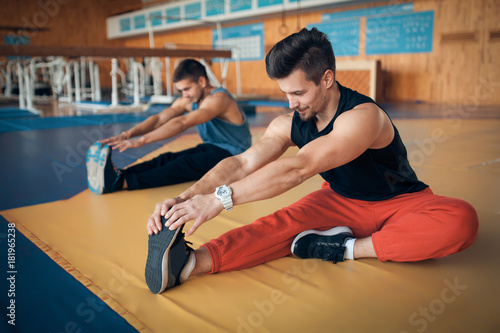 two young handsome guys stretching in oldschool gym;