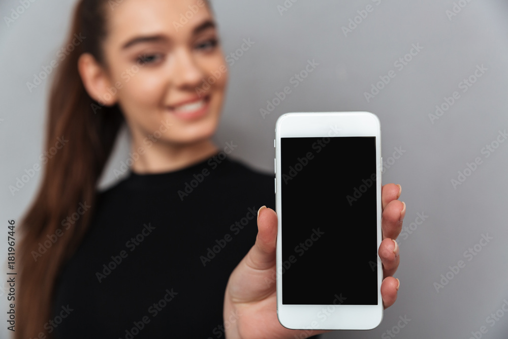 Happy brunette woman in black clothes showing blank smartphone screen