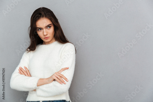 Close-up photo of upset brunette girl in soft sweater standing with crossed hands, looking aside