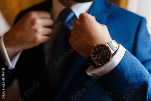 The man in the blue suit straightens his jacket. Businessman in classic suit with expensive watches. Businessman in white shirt, blue tie and jacket. Closeup