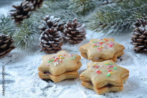 Close up of traditional bulgarian double cookies, called "medenki", with jam filling and colorful sticks icing on a snow like powdered sugar background with pine cones and twigs