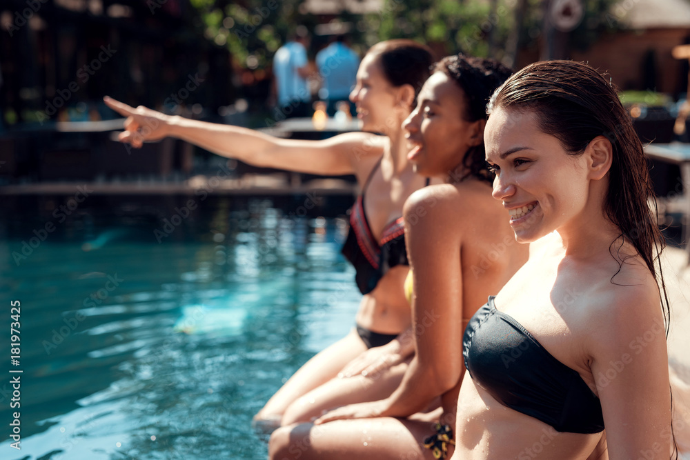 Girls in a bikini sit on the edge of the pool.