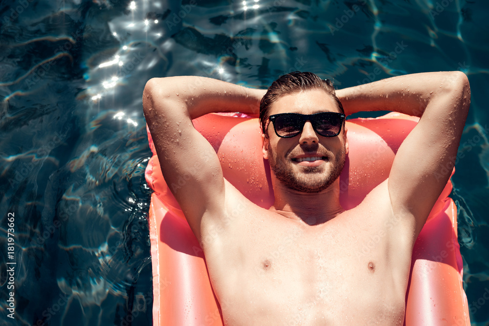 A guy in sunglasses is floating on an inflatable mattress in the pool.