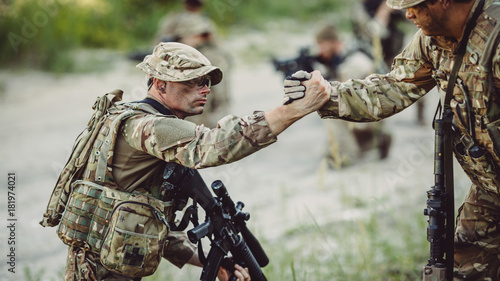 rangers during the military operation. soldiers climbing on mountain, one of them giving hand and helping to climb. Help, support, assistance in a dangerous situation