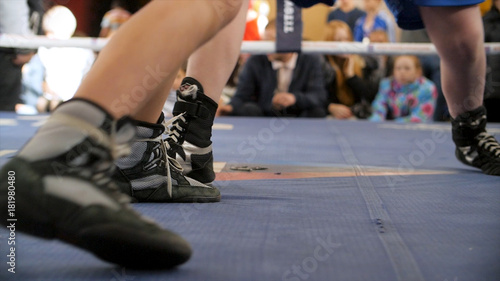 Two boxers fight in the boxing ring in boxing shoeses. Low section of male boxer standing against referee by athlete lying in boxing ring