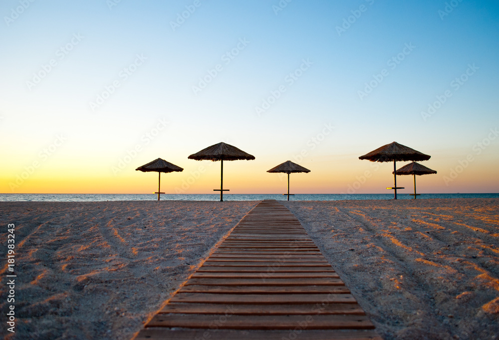 several a lot of big beach umbrellas made of straw and metal stand on the sea shore trail of wood path sand beach blue sea blue sky summer morning evening calm several a lot of big beach umbrellas made of straw and metal stand on the sea shore trail of wood path sand beach blue sea blue sky summer morning evening calm