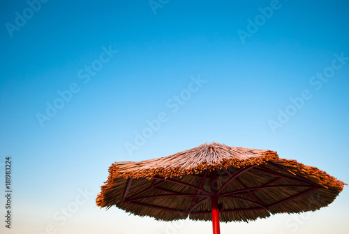 large beach umbrella made of straw and metal on a background of empty clean blue sky summer morning weekend vacation