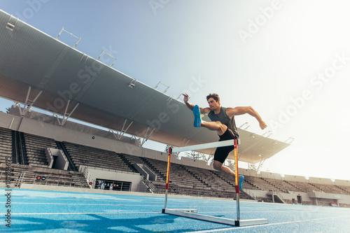 Athlete jumping over an hurdle on running track