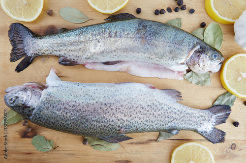 Horizontal shot of trout arranged on a wooden board surrounded by spices and lemon slices.   photo