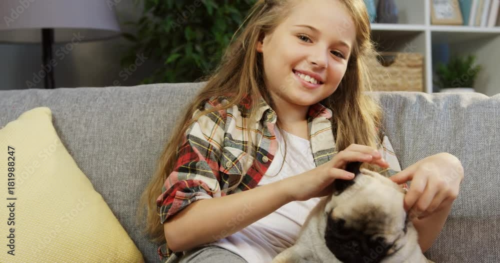 Portrait of a cute blonde 10 years old girl hugging a pug and smiling on the couch at home. Indoors Portrait of a cute blonde 10 years old girl hugging a pug and smiling on the couch at home. Indoors