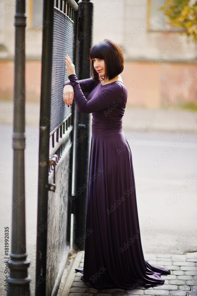 Adult brunette woman at violet gown background black iron gates.