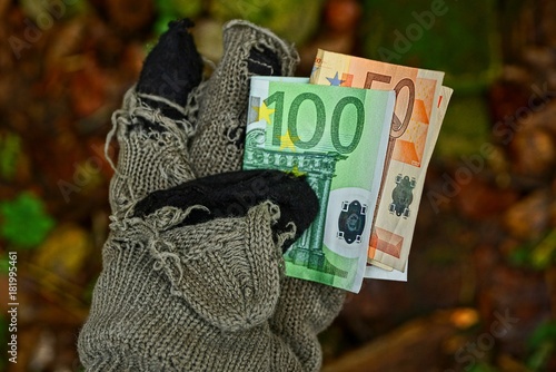 бездомный держит бумажные деньги в рваной шерстяной перчатке