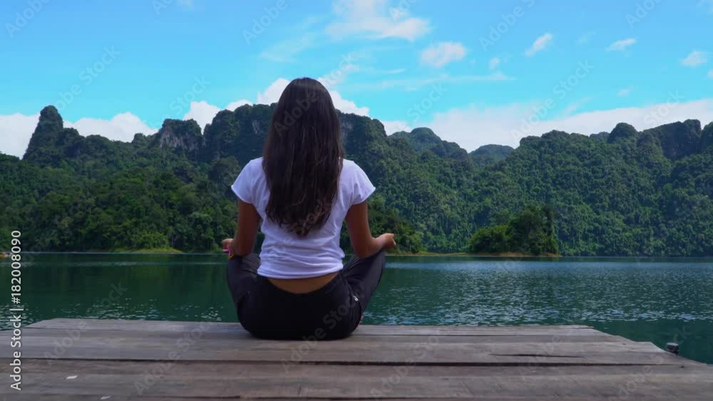 A girl sits on a pier in a lotus pose on a lake with a beautiful view. Cheow Lan lake. Khao Sok National Park. Thailand. A girl sits on a pier in a lotus pose on a lake with a beautiful view. Cheow Lan lake. Khao Sok National Park. Thailand.