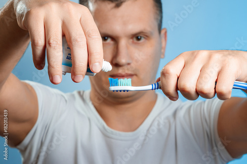 Close up of an attractive young man brushing his teeth. A man squeezes toothpaste into a toothbrush. Focusing on tools. The concept of oral hygiene.