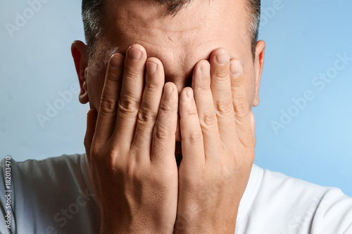 Wallpaper Mural White man, close-up portrait, covered his face with his hands on a blue background. Torontodigital.ca