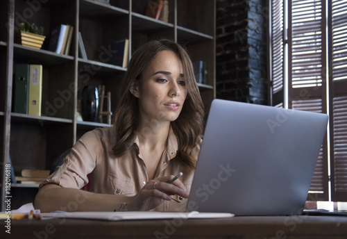 Young beautiful business woman working with laptop at table near window