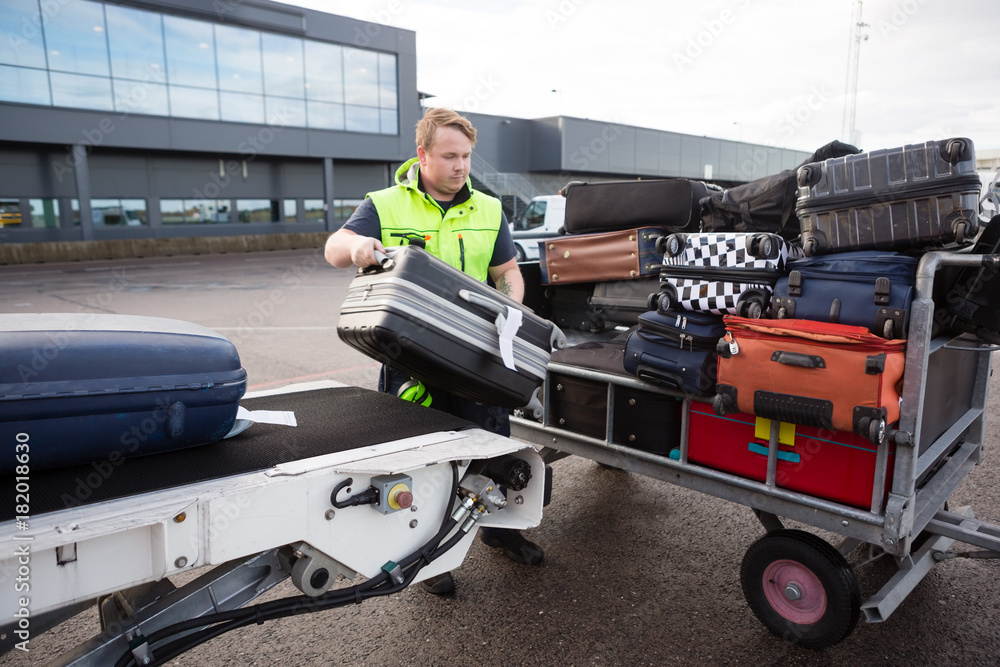 Fotografie Worker Stacking Luggage On Trailer From Conveyor On Runway
