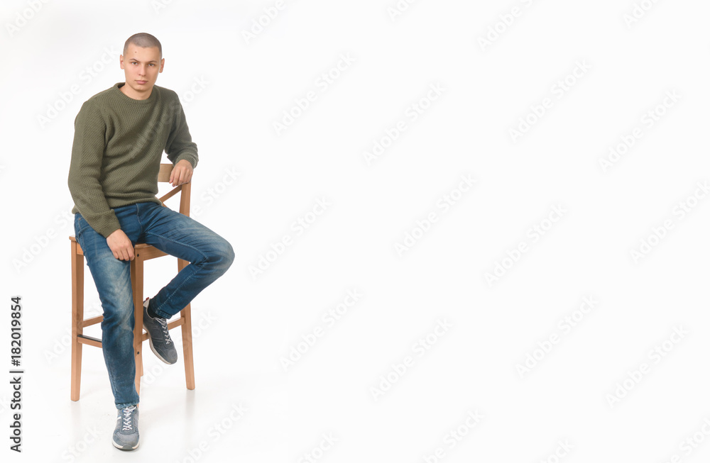 A young man is a skinhead in a green military style sweater. Studio. the guy sits on the boxes A young man is a skinhead in a green military style sweater. Studio. the guy sits on the boxes